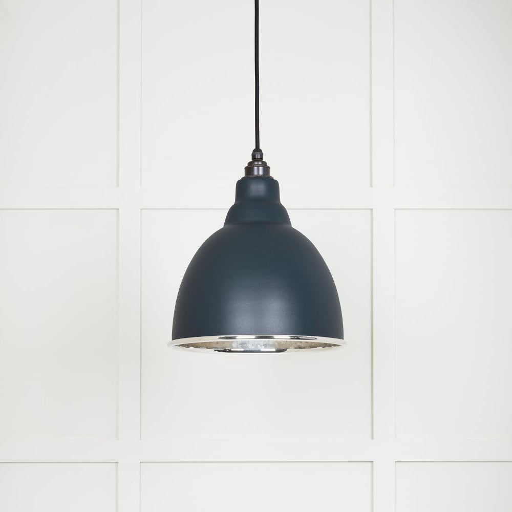 Hammered polished nickel Brindley pendant light in soot hanging from a black fabric cable against a white panelled wall