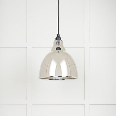 Hammered polished nickel Brindley pendant light hanging from a black fabric cable against a white panelled wall