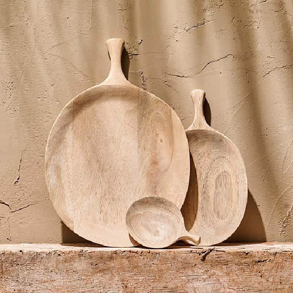 Carved mango wood serving platters with slimline handles in 3 different sizes  leaning up against a sand coloured textured wall