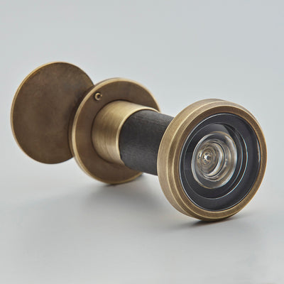 Solid brass door viewer in light antique finish from the front angle on a white surface
