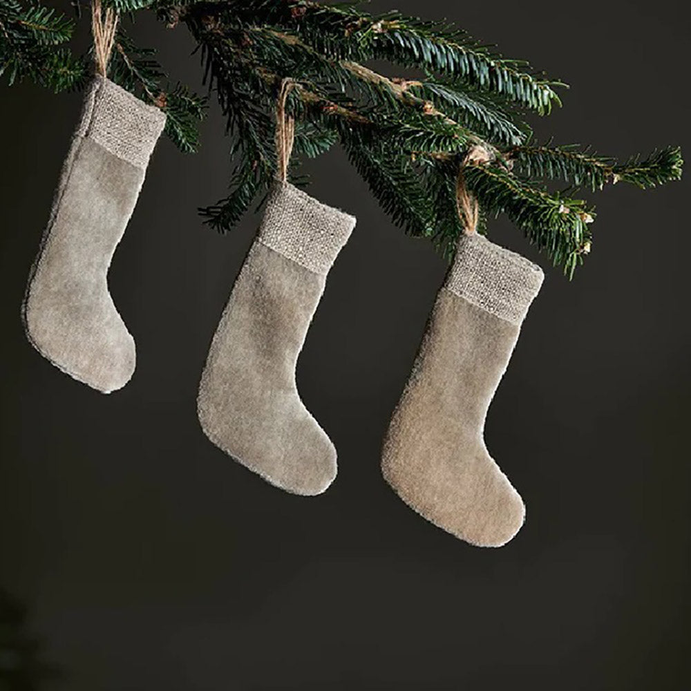 Light grey set of 3 mini stocking decorations made from velvet with a jute linen band at the top. Hanging from jute rope on a christmas tree against a dark blue background