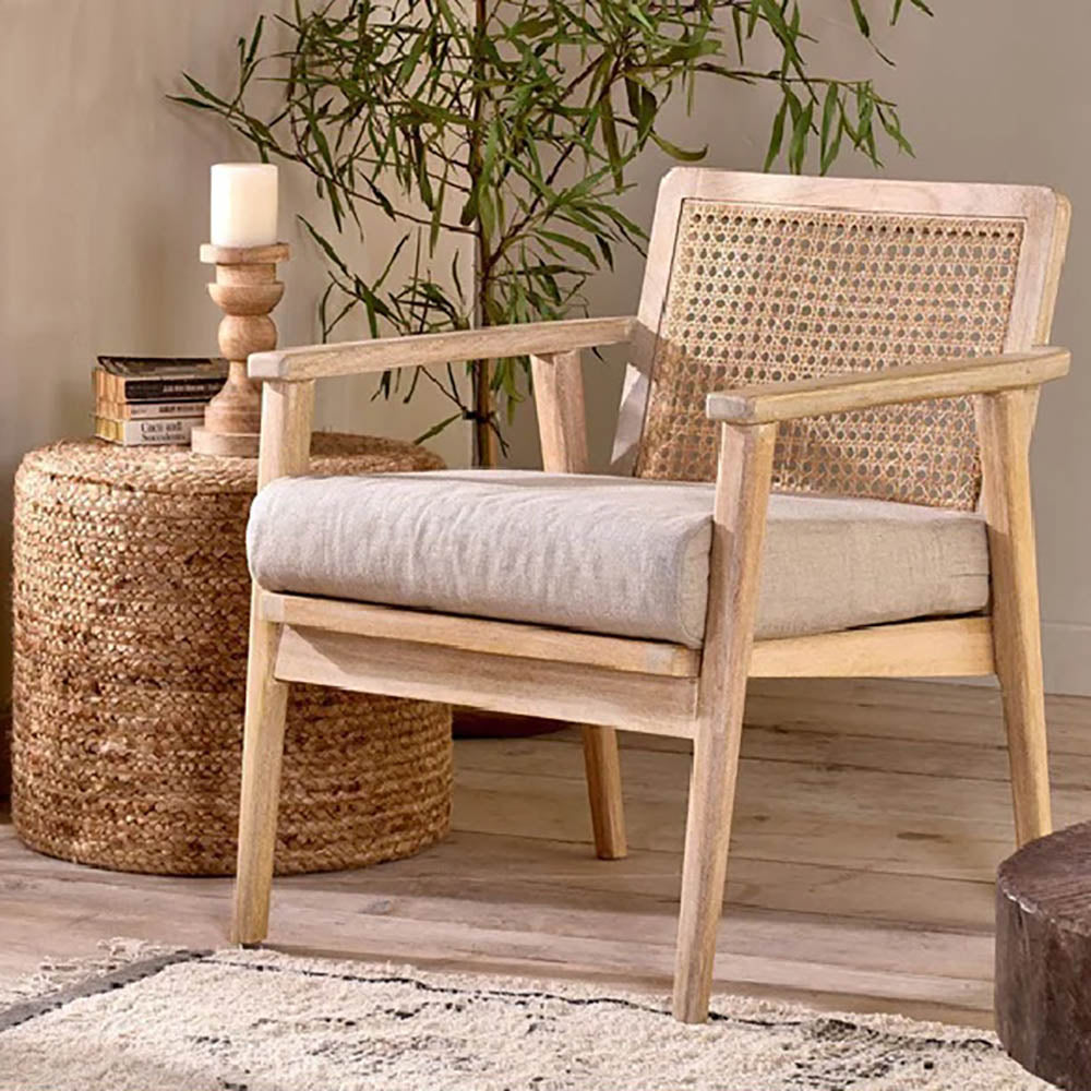 Mango wood occasional chair with linen cushion on wooden floor next to a rattan table and large plant