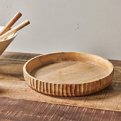 A view of the inside of a mango wood shallow serving bowl with a flat base and hand carved etching around the outer edge, sitting on a wooden table.