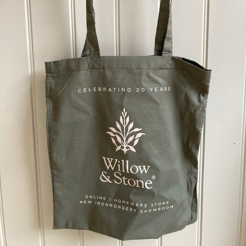 Olive green tote bag with 'Willow & Stone' logo hanging on a wooden rack against a white panelled wall.