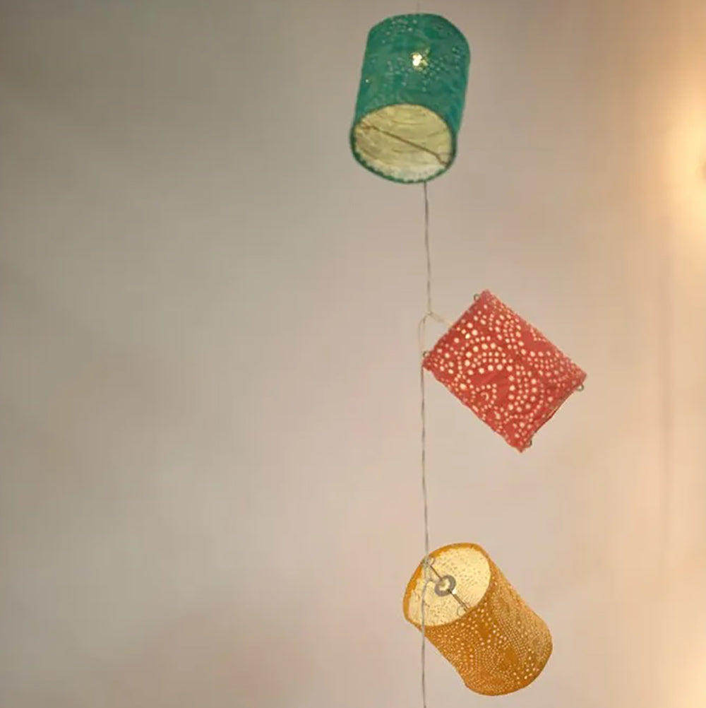 Teal, yellow and pink paper lanterns, illuminated, hanging against an off-white wall