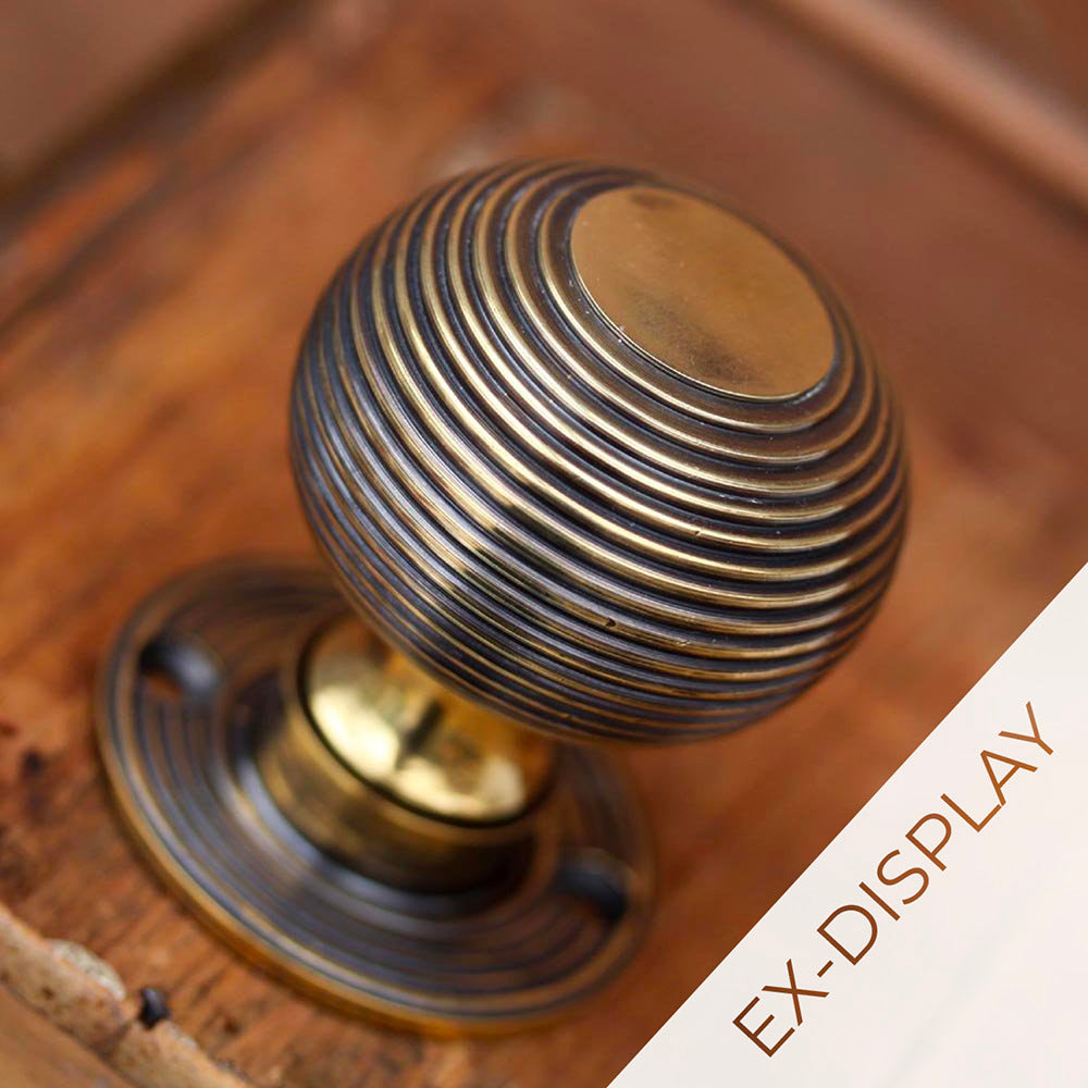 Solid brass door knob with an antique finish and reded beehive detailing on a wooden background