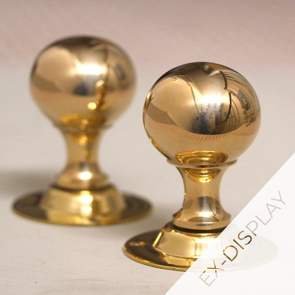 Pair of polished brass round door knobs on a pale pink background with a watermark and ex display text in the corner