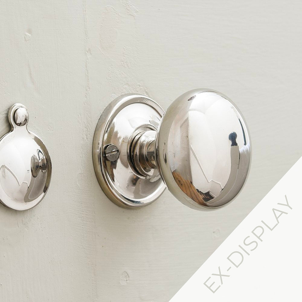 Polished nickel cottage bun door knobs with a round polished nickel escutcheon on a beige background with an ex-display watermark in the corner