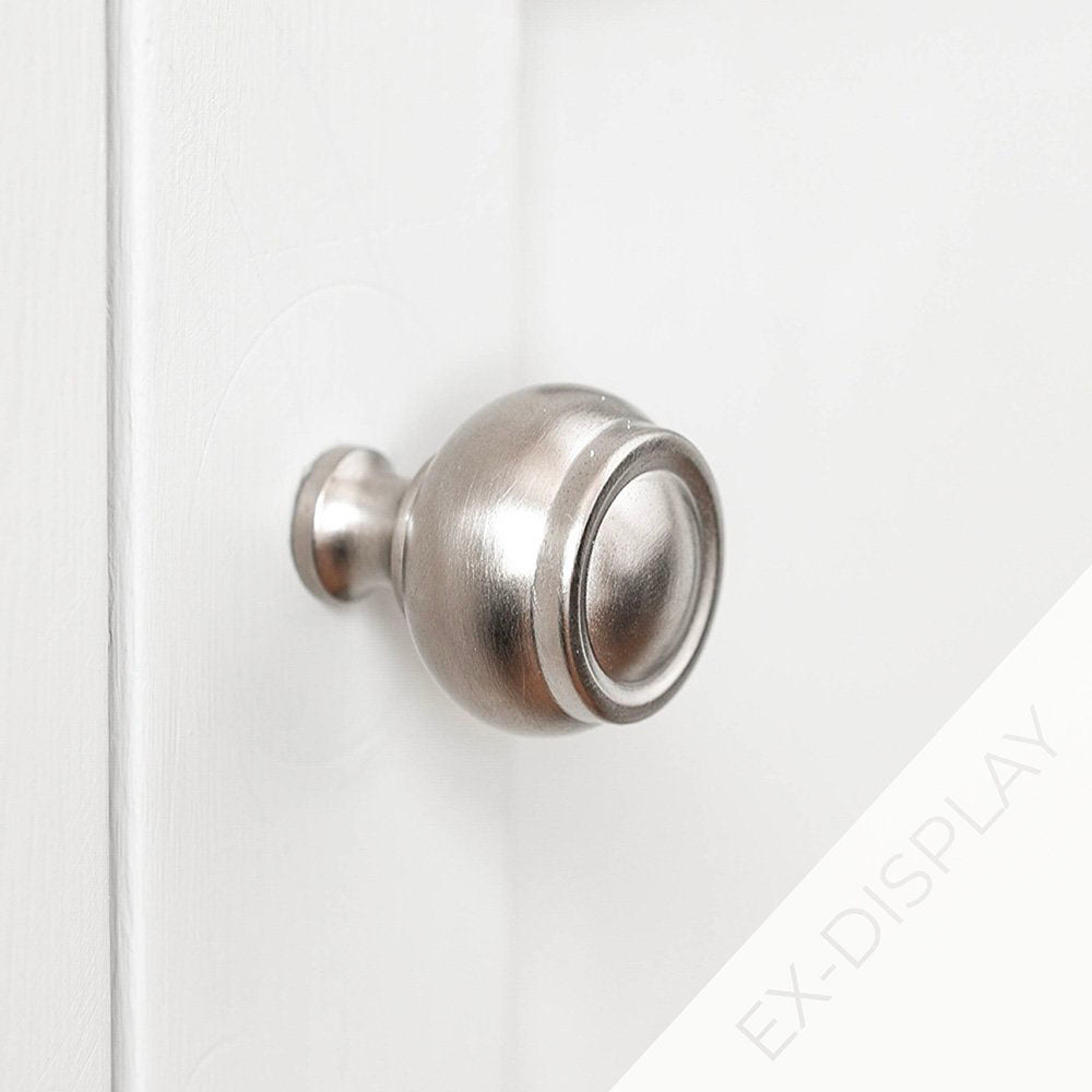 Small round satin nickel cabinet knob with ridged detailing to the top on a pale grey background with an ex-display watermark in the corner