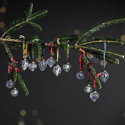 Set of 12 recycled glass baubles in a mix of round and teardrop designs with clear glass and silver crackle finishes. They hang from a christmas tree branch with coloured ribbons  against a dark blue background