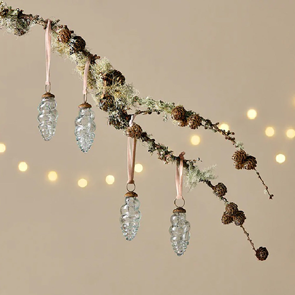 Set of 4 clear glass teardrop baubles in a shell-like design with light pink velvet ribbon hanging from a branch against a pale yellow background