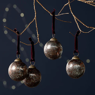 Set of 4 glass baubles in a rustic antique burgundy finish with deep red velvet ties haning form copper wire against a dark blue background