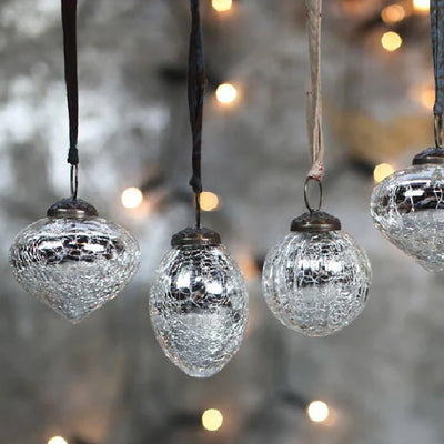 Set of 4 silver crackle glass baubles hanging from patterned ribbons against a blurred out grey and fairy light background
