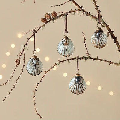 Set of 4 white and gold glass shell baubles with pink velvet ribbon hanging from a tree branch against a pale yellow background