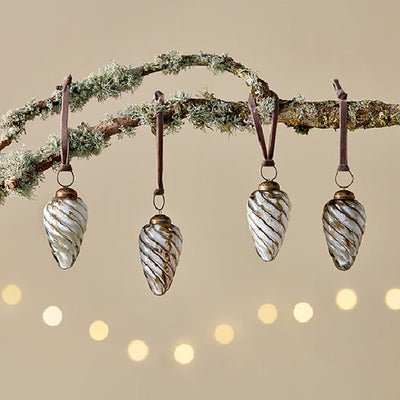 Set of 4 white and gold teardrop glass baubles in a shell like design with pink velvet ribbon hanging from a tree branch against a pale yellow background