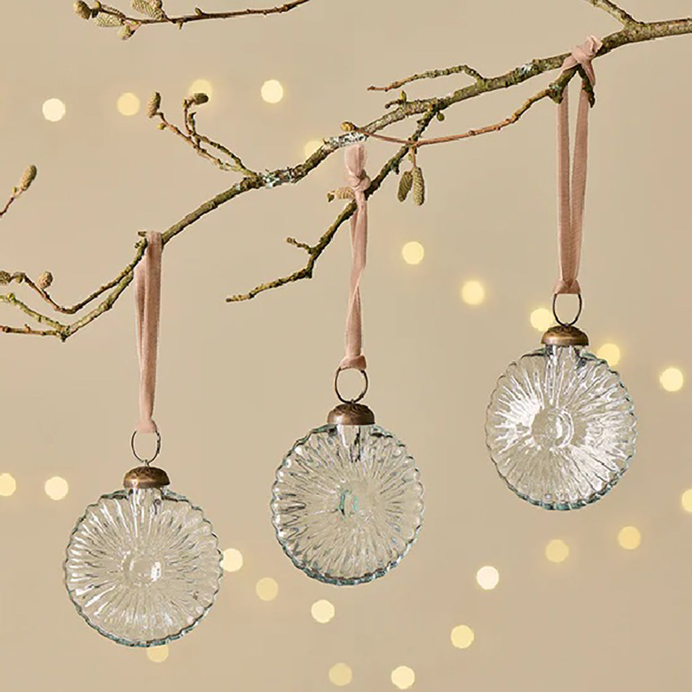 Set of vintage style clear glass baubles in a fossil inspired design hanging from a branch with light pink velvet ribbon