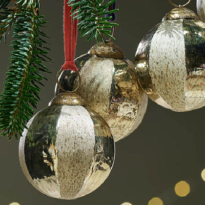 Close up of gold glass baubles with etched detailing hanging from a christmas tree branch with different coloured ribbon against a dark green background