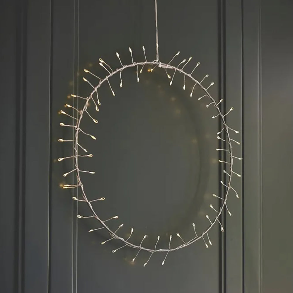 Warm white LED fairy light hoop on a silver wire frame hanging against a dark green wall