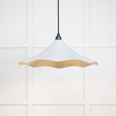 Smooth brass flora pendant light in birch hanging from a black fabric cable against a white panelled wall