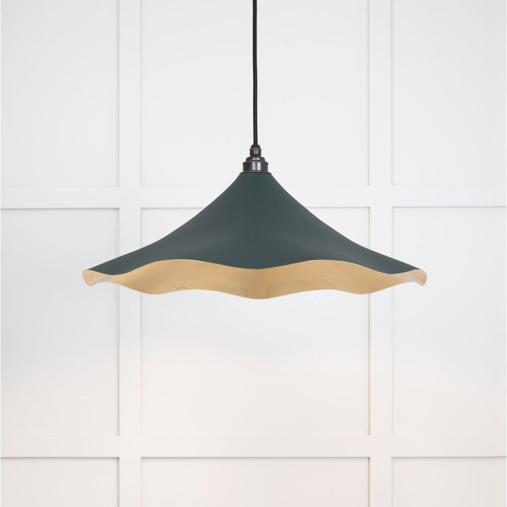 Smooth brass flora pendant light in dingle hanging from a black fabric cable against a white panelled wall