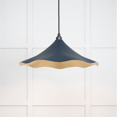 Smooth brass flora pendant light in dusk hanging from a black fabric cable against a white panelled wall