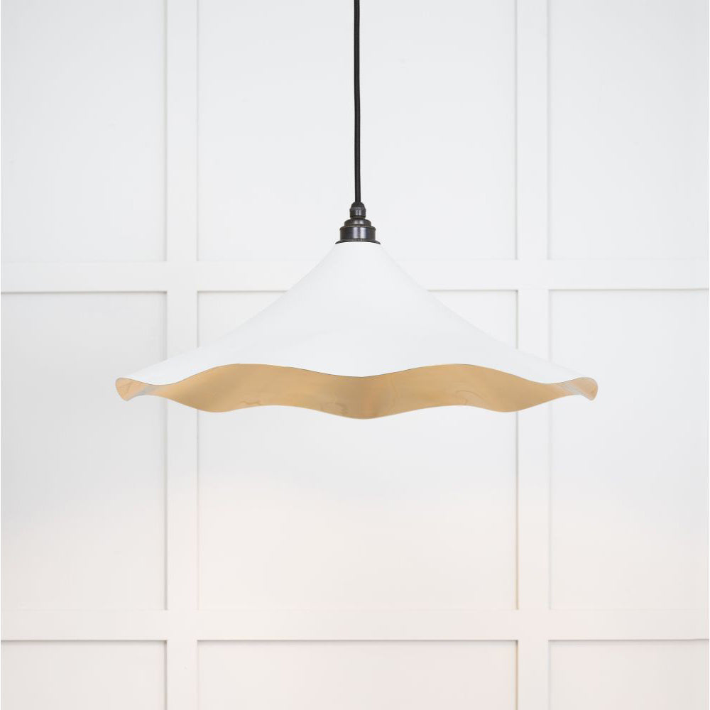 Smooth brass flora pendant light in flock hanging from a black fabric cable against a white panelled wall