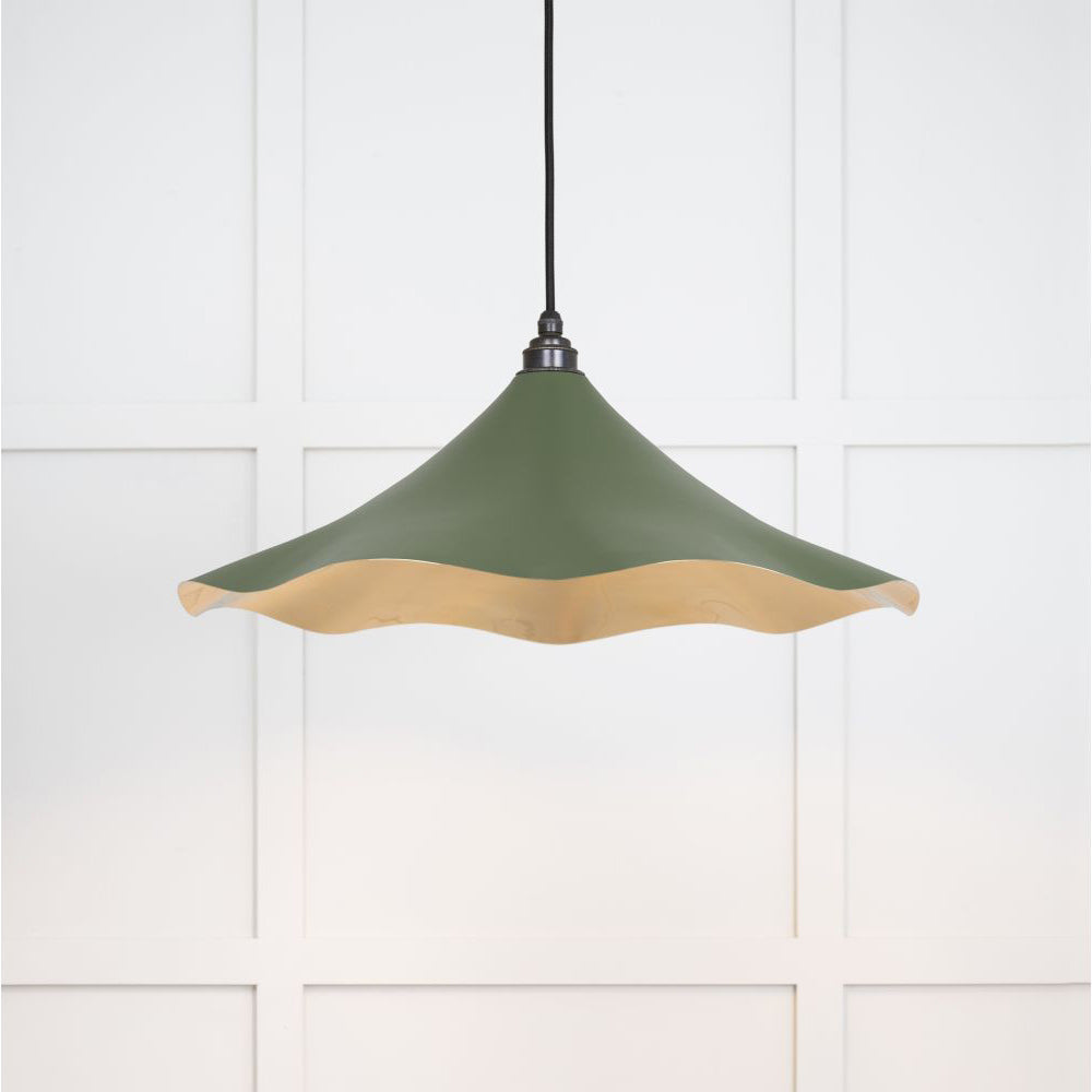 Smooth brass flora pendant light in heath hanging from a black fabric cable against a white panelled wall