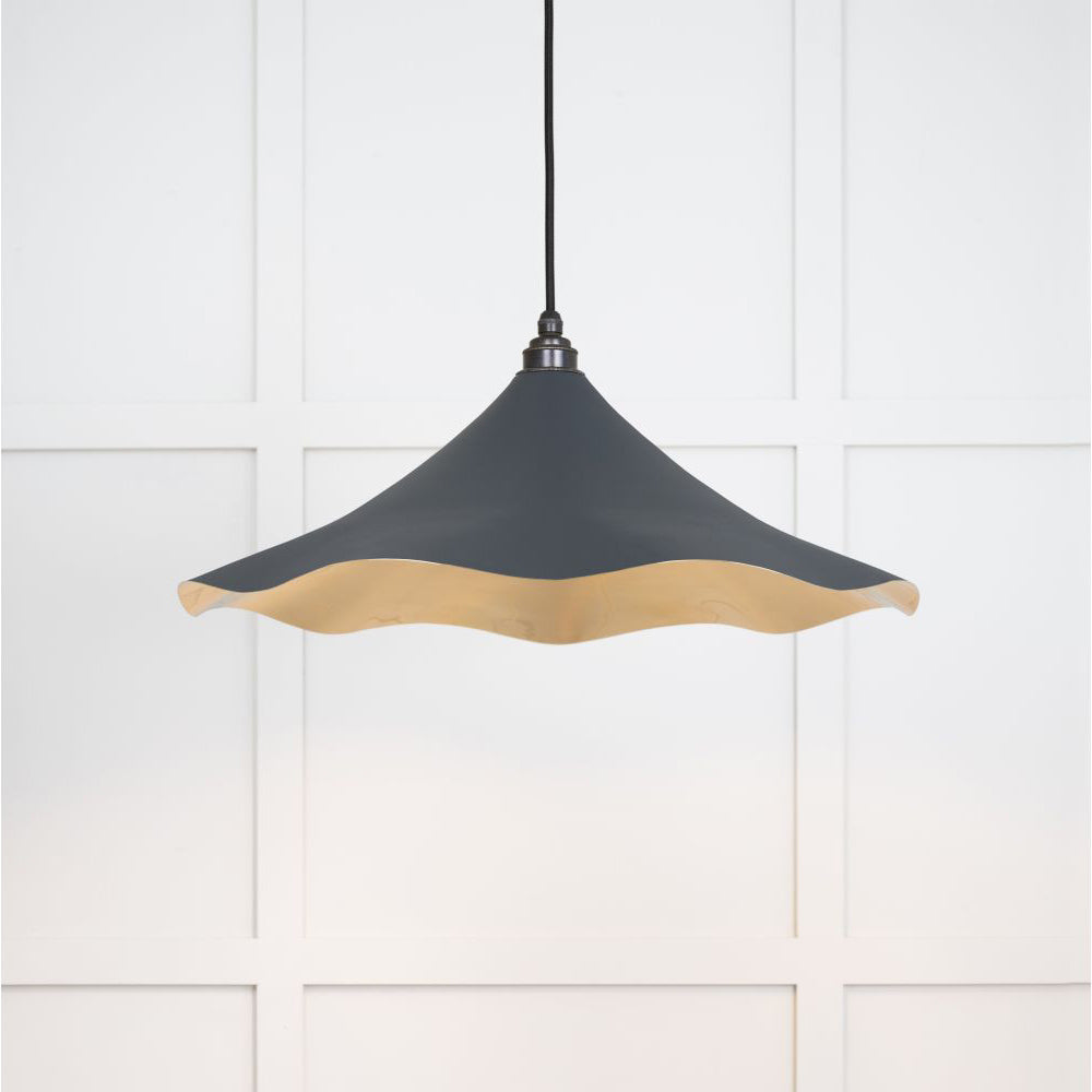 Smooth brass flora pendant light in soot hanging from a black fabric cable against a white panelled wall