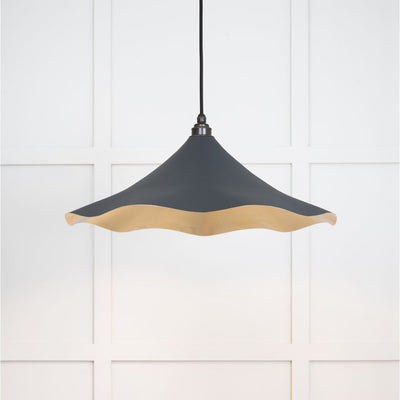 Smooth brass flora pendant light in soot hanging from a black fabric cable against a white panelled wall