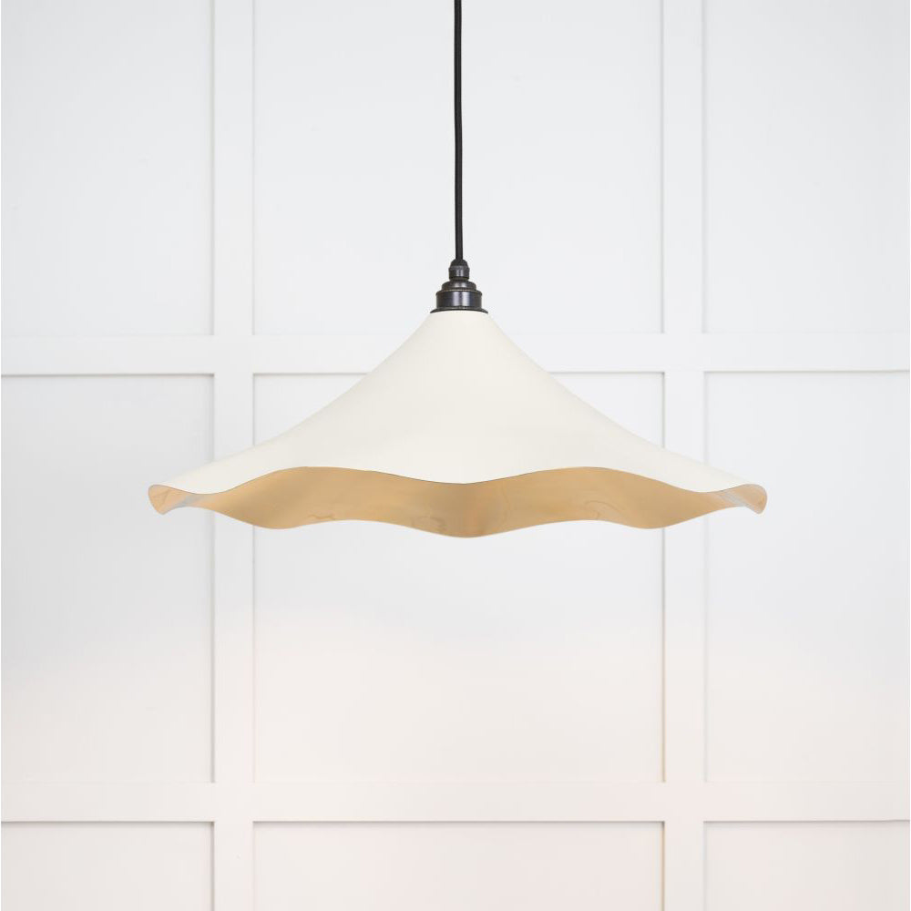 Smooth brass flora pendant light in teasel hanging from a black fabric cable against a white panelled wall