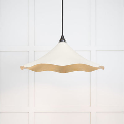 Smooth brass flora pendant light in teasel hanging from a black fabric cable against a white panelled wall