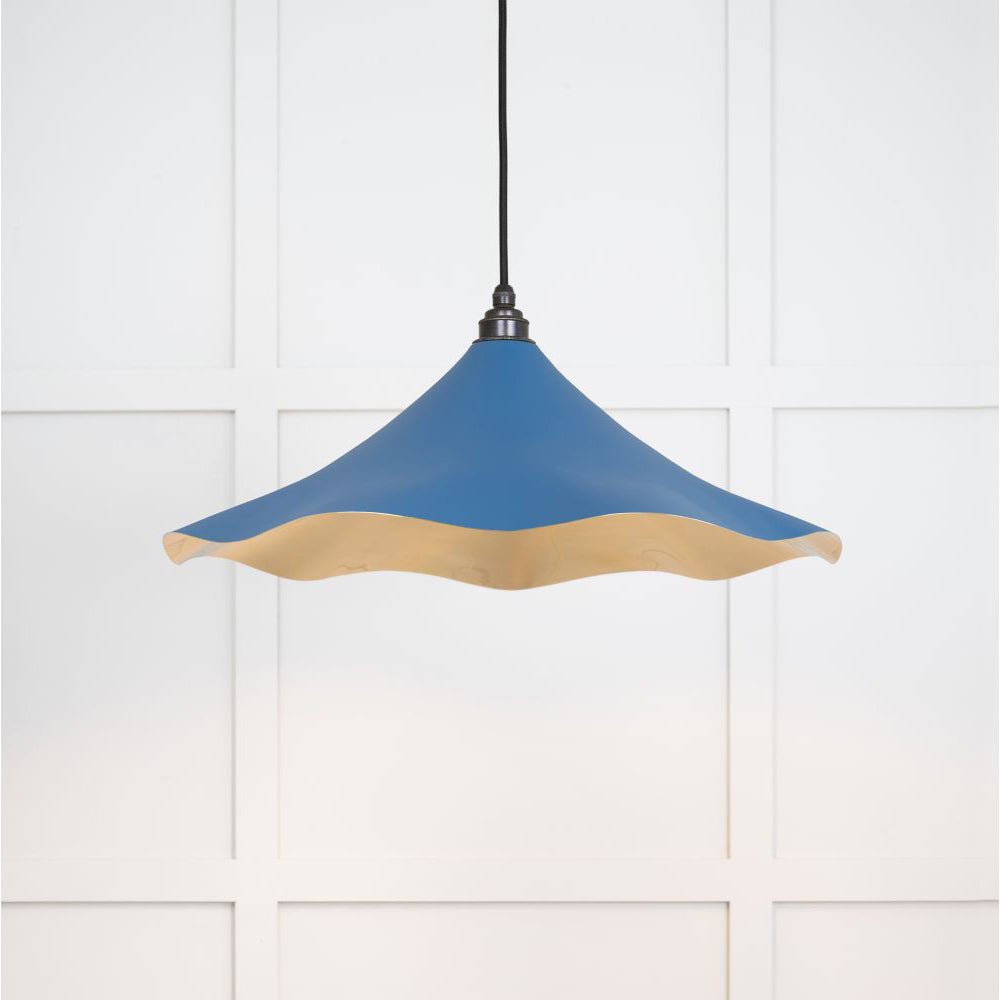 Smooth brass flora pendant light in upstream hanging from a black fabric cable against a white panelled wall