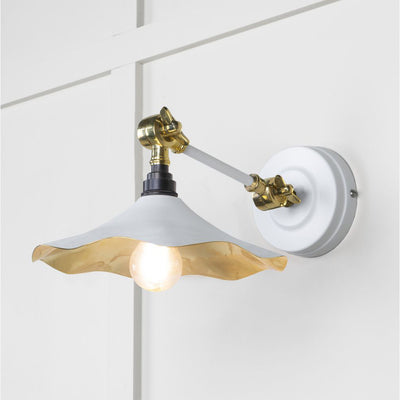 Smooth brass flora wall light in flock against a white panelled wall