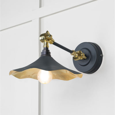 Smooth brass flora wall light in soot against a white panelled wall
