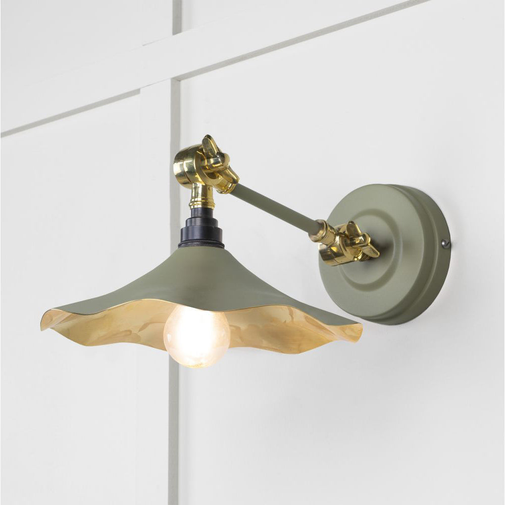 Smooth brass flora wall light in tump against a white panelled wall