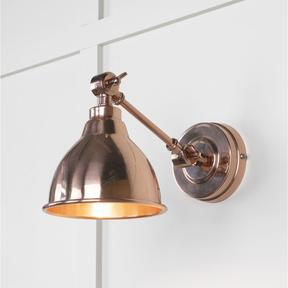 Smooth copper wall light, lit up against a white panelled wall