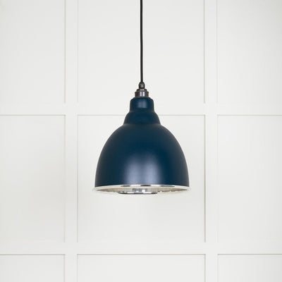 Smooth polished nickel Brindley pendant light with a powder coated finish in dusk hanging from a black fabric cable against a white panelled wall