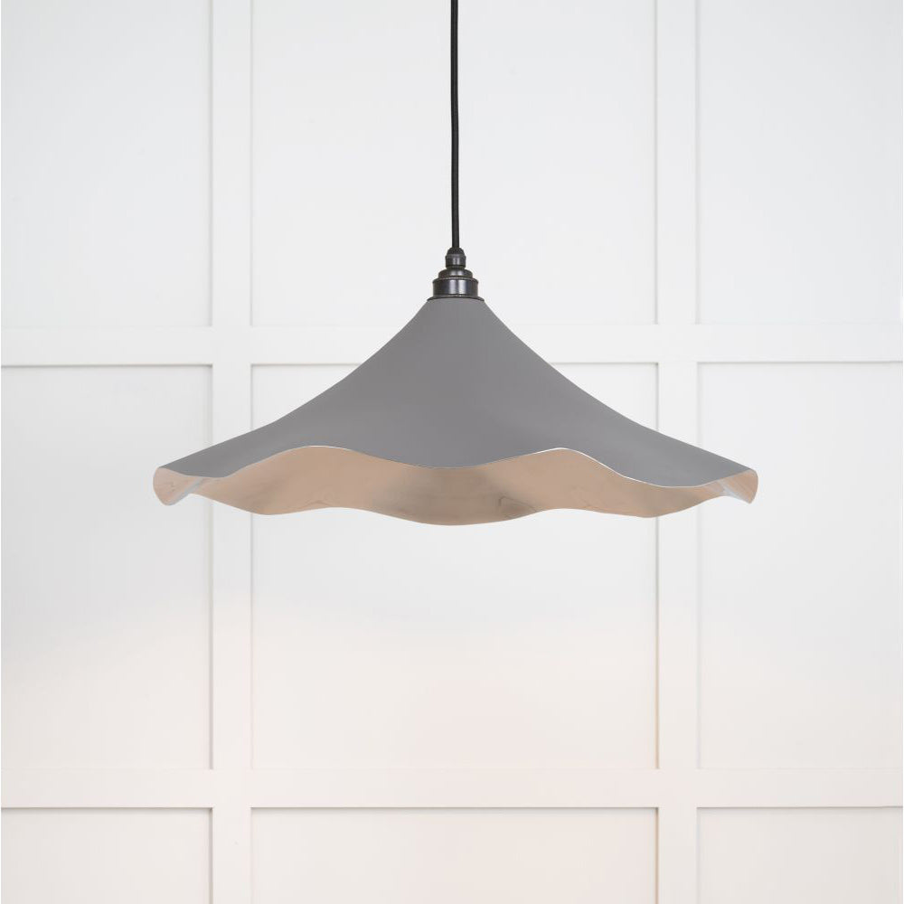 Smooth nickel flora pendant light in bluff hanging from a black fabric cord against a white panelled wal