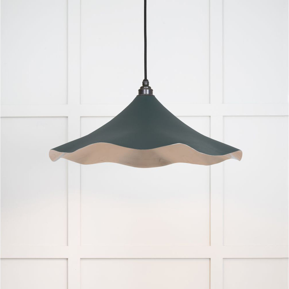 Smooth nickel flora pendant light in dingle hanging from a black fabric cord against a white panelled wal