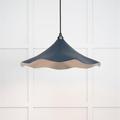 Smooth nickel flora pendant light in dusk hanging from a black fabric cord against a white panelled wal