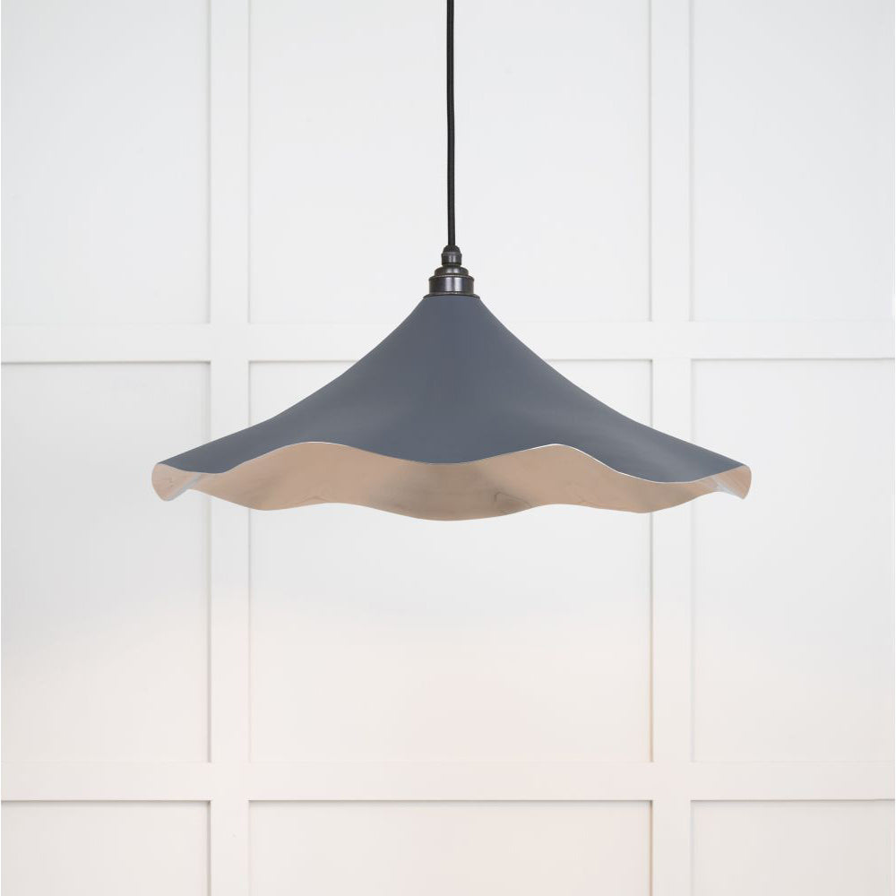 Smooth nickel flora pendant light in slate hanging from a black fabric cord against a white panelled wal