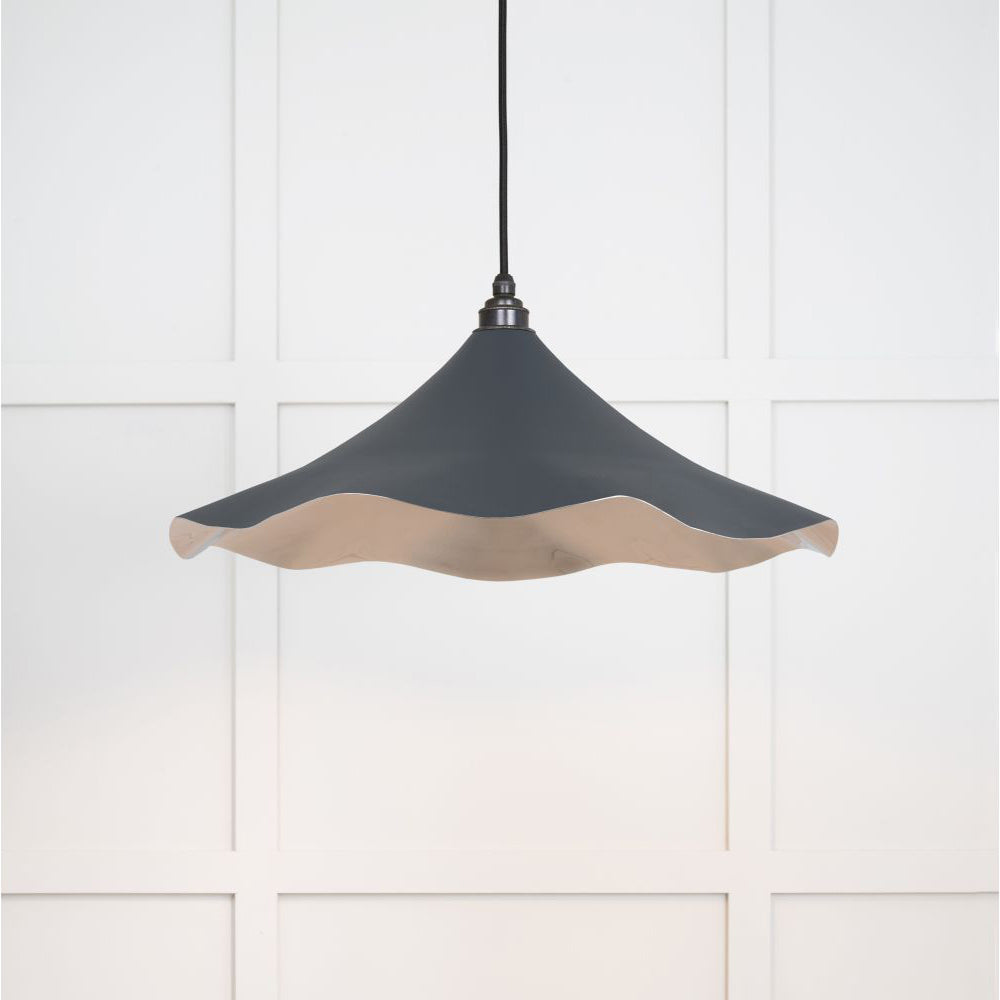 Smooth nickel flora pendant light in soot hanging from a black fabric cord against a white panelled wal
