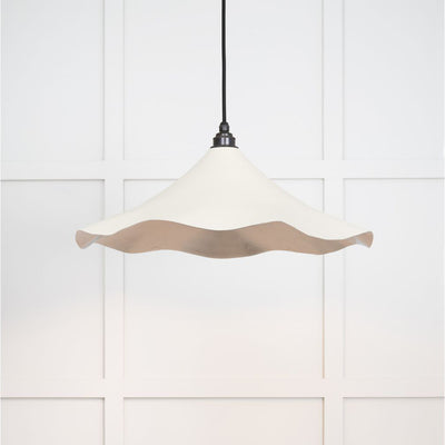 Smooth nickel flora pendant light in teasel hanging from a black fabric cord against a white panelled wal