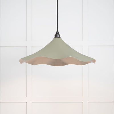 Smooth nickel flora pendant light in tump hanging from a black fabric cord against a white panelled wal