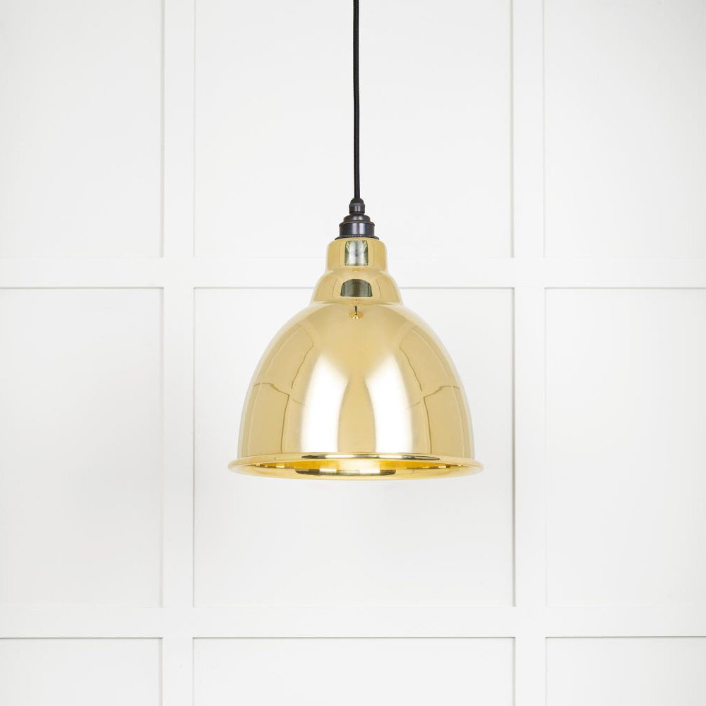 Smooth polished brass Brindley pendant light hanging from black fabric cable against a white panelled wall