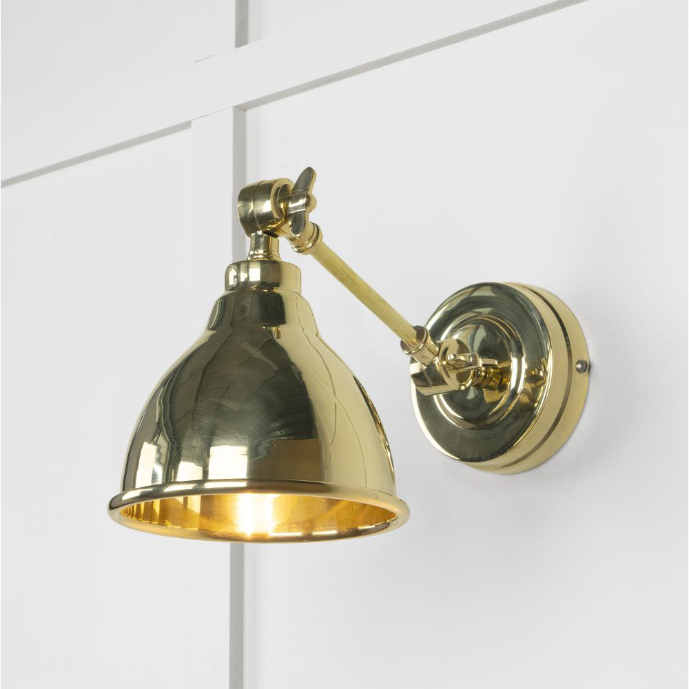 Polished brass wall light, lit up against a white panelled wall