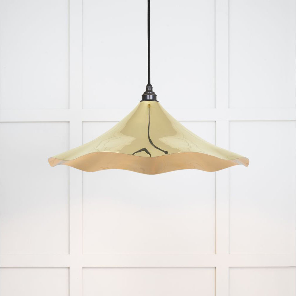 Smooth polished brass flora pendant light with a black fabric cord against a white panelled wall