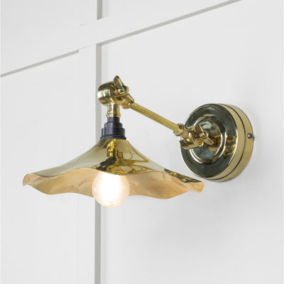 Smooth polished brass flora wall light against a white panelled wall