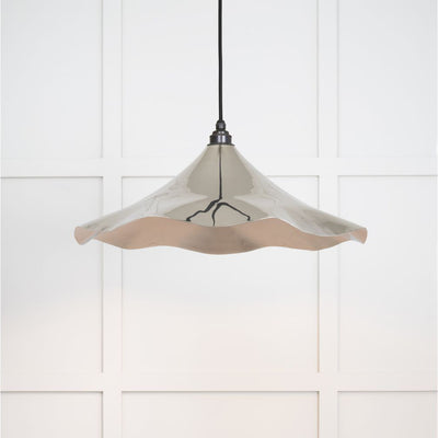 Smooth polished nickel flora pendant light hanging from a black fabric cord against a white panelled wall