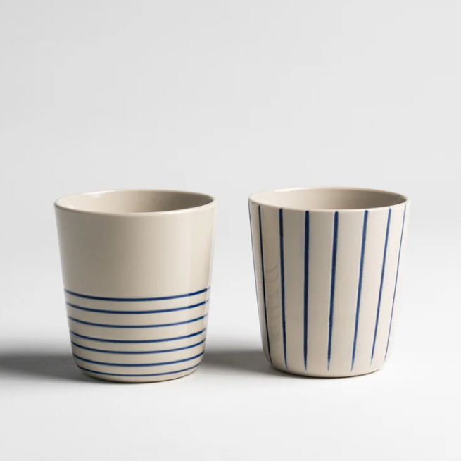 Two ceramic cups with blue stripes on a light gray background